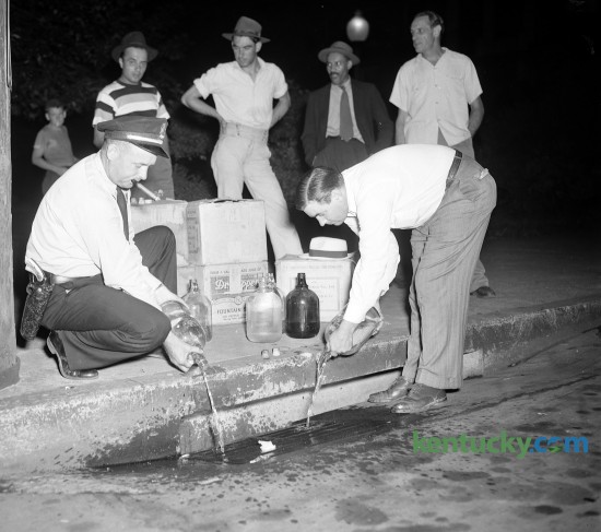 County Patrol Lt. Frank Dillon, left, and Patrol Chief Walter Franklin pour confiscated moonshine whiskey down the sewer, July 1948.