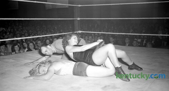 Action picture of women's wrestling match at Woodland auditorium. Nell Stewart, blonde, with Violet Viann applying a variation of the toehold. Frank Bunch, referee. 11/5/1946 There was an auditorium built near the center of the park in the 1880’s that was used for concerts, conventions and other public meetings. In October 1905, the frame auditorium was replaced by a large brick one that stood at the northeast corner of Kentucky Avenue and East High Street. http://kentuckyroom.org/subject-headings/wrestling