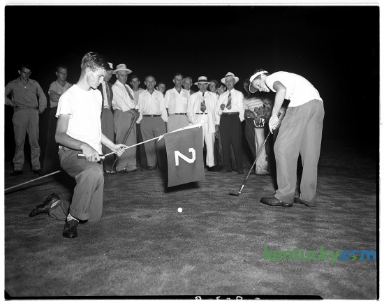 John Y. Brown Jr. putts in darkness while his opponent, John Williams held a flashlight and the flag during the Lexington City Golf Tournament Aug. 19, 1948. In the background above the flag is Brown's father John Y. Brown Sr., wearing a white suit and hat. The senior Brown was an attorney and politician, serving one term in the U.S. House of Representatives from 1933-35. His son was governor of Kentucky from 1979-83. At the time of this picture, John Y. Brown Jr. was a student at Kentucky Military Institute.