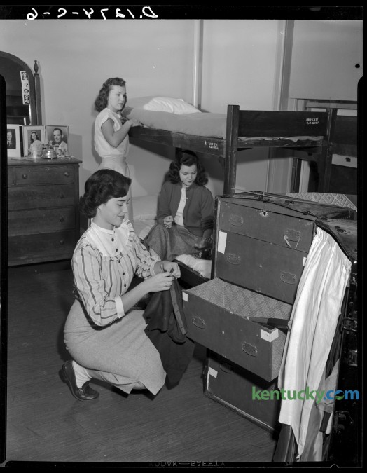 University of Kentucky coeds moved into their dorm room in Patterson Hall during orientation week activities.  Pat Moore, foreground, unpacks,  Marian Ferguson, rear,  made up her bunk and Mary Jo Cundiff applied polish to her nails.  Published in the Herald-Leader September 18, 1949. 