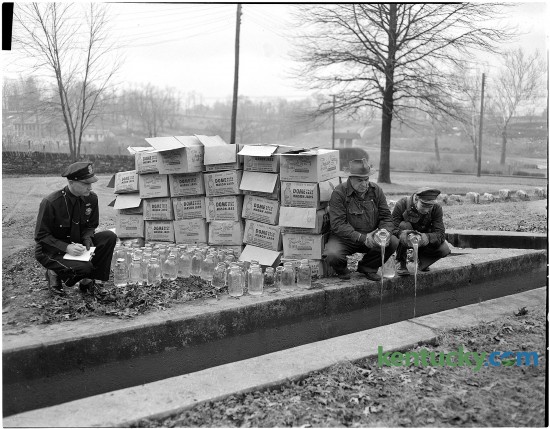 Patrolman Lloyd Lindsey watching two city workhouse prisoners pour moonshine whiskey that was confiscated by police into the sewer. Published in the Lexington Herald Jan. 11, 1951.