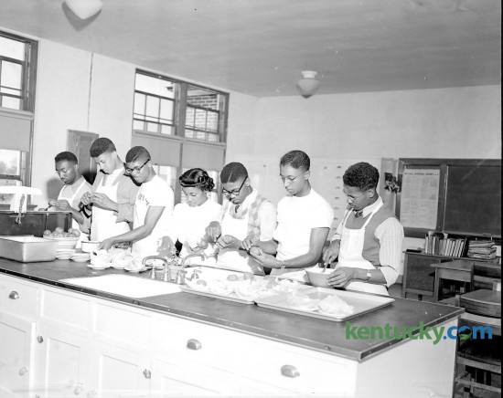 With their instructor, Mattie Ballew, six of the 12 boys enrolled in a home economics class at Douglass school prepare food for a father-son banquet that was held on a Friday night in May 1949. The Home-ec class for boys, started in January as an experiment, had become so popular it was added to the regular curriculum, and included planning and preparing meals, household management and family relationships. Shown in the photo (left to right) are Demosthenes Hunn, Augustus Mack Jr., Rupert Seals, Miss Ballew, Walker Green, Jesse Yates and Murray Cruse. Photo appeared in the Sunday Lexington Herald-Leader May 8, 1949.