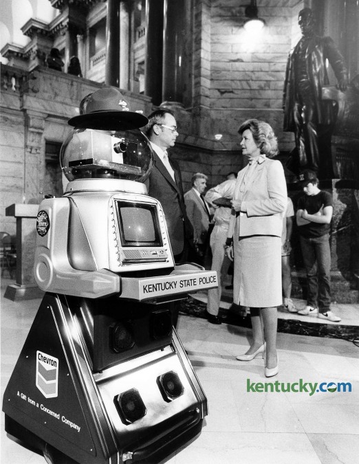 A robot was sworn in as a Kentucky State Trooper Aug. 6, 1984 at the state capital in Frankfort. The robot, which was donated by the Chevron Corp. at a cost of $14,750, was used to teach traffic safety in Kentucky schools. The robot was sworn in by Kentucky Chief Justice Robert F. Stephens and given badge No. 219. In the background, Kentucky State Police Commissioner Morgan T. Elkins and Gov. Martha Layne Collins talk in the capitiol rotunda. The governor tried to be kind during ceremony. "I'm saying he, but we'll let that go," she said. Stephens was even a bit more serious that the occasion may have demanded when he called for the officer candidiate to repeat the oath of office. Following Stephens' lead, the robot promised to "promote the peace and safety of this commonwealth, to serve mankind by responding to the needs of you humanoids... to the best of my ability, batteries and computer willing." Chevron provided a $500 savings bond that will go to the winner of a contest to name the newest trooper.  Photo by David Perry | staff
