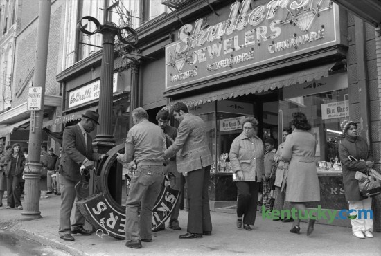 Employees of Skuller's Jewelry, 115  West Main Street, prepared to move the huge frame of the street clock  that had fallen to the sidewalk Monday January 28, 1974 after strong winds knocked it off it's pole, injuring Carolyn Green of Falmouth. The clock dates back to 1913, when Skuller's jewelry store had the clock built to advertise their company. The cast-iron  clock, which is about 14 feet tall, was taken down in 2010 and stored until funds were raised for the complete restoration by the Verdin Company of Cincinnati. The clock was rededicated in September or 2013.  Photo  by Ron Garrison | Staff