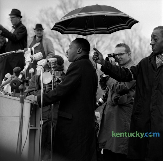 The Rev. Dr. Martin Luther King, was sheltered by an umbrella from the rain as he addressed some 10,000 people who attended a rally in Frankfort at the State Capitol on March 5, 1964. Photographer Bill Strode, center, was on assignment for the Louisville Courier Journal. 