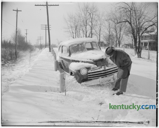 Howard Lovely, a salesman from Paintsville examined his automobile stuck in the snow on the Nicholasville Pike in February 1947. Published in the Lexington Herald February 5, 1947. 