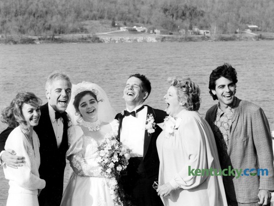 The wedding of Adelia "Ada" Clooney and Norman Zeidler, center, included this moment with Clooney family members March 14, 1987 on the banks of the Ohio River in Augusta, Ky. From left, Nina and her husband, Cincinnati WKRC-TV anchorman Nick Clooney, their daughter and new son-in-law, Nick's sister, Hollywood star Rosemary and bride's 26-year-old brother, actor Grorge. The wedding was a hometown affair. A roll of fence wire, tied with gift ribbons, marked off the curb in front of the Clooneys' Victorian frame house. Local friends with 1918 Model T and other vintage cars drove the wedding party two blocks to St. Augustine Catholic Church and four blocks to the riverfront reception. Before the nuptial Mass, Rosemary sang a non-religious song of love and dedication, "The Promise," for "only the second time I've sungit," said the Concord Jazz recording star. "The first time I sang it was to my son (Gabriel Ferrer) when he married Debby Boone." George read from The Song of Solomon, Psalms and Revelations in the wedding service. Outside the church, surrounded by a circle of seven girls, the actor said he couldn't remember the name of his role in that night's episode in the television series "Murder, She Wrote." "I played 'Kip' -- I think -- but it was filmed 1 1/2 months ago," George said. Said the mother of the bride, "The whole town" of Augusta, population 1,500 -- "helped with the wedding. We couldn't have gotten through it without them." The city blocked off Parkview Street, which dead-ends at the river, for a tent to be set up for the reception for 300. The road surface was the dance floor for swinging to the seven-piece Jerry Conrad's Rhythm & Brass band from Cincinnati. Photo by Jocelyn Williams