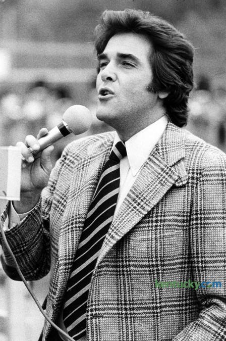 Television personality Chuck Woolery sings "My Old Kentucky Home" during halftime of the Morehead State football game Oct. 15, 1977 in Morehead. Woolery, a Morehead State alumnus, was the original host for the game show Wheel of Fortune. He also hosted (more than 2,000 episodes) Love Connection, Scrabble, The Home and Family Show, The Chuck Woolery Show, The Dating Game, Greed and Lingo. Woolery who was born in Ashland, studied economics and sociology at Morehead. Photo by David Perry | staff