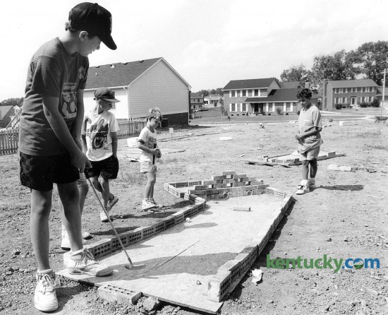 Neighborhood kids along Stone Creek Drive in south Lexington Aug. 12, 1991 decided to turn a vacant lot into a miniature golf course using scrapes of lumber, bricks and plastic pie from a nearby trash pile. Pictured is Nicholas McClure, 11, hitting his shot as from left Morgan, Smith, 9, Andy Farmer, 7, and David Lovejoy, 11, watch. Photo by Ron Garrison | staff