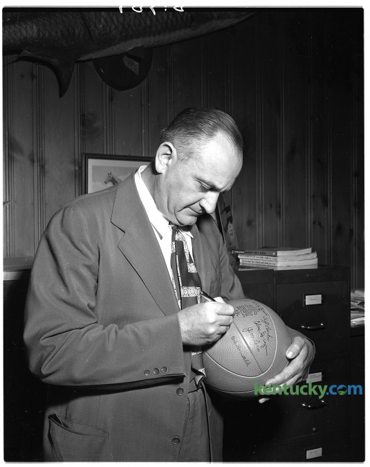 Legendery University of Kentucky basketball coach Adolph Rupp autographs a basketball that will be awarded to youth organizations in state for the sale of E bonds. Published in the Lexington Herald-Leader June 26, 1949. Herald-Leader Archive Photo