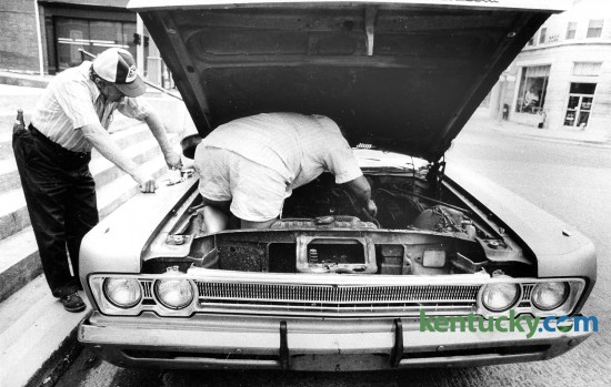 Russell Templin went right to work on his car, Aug. 17, 1985, after it broke down on Main Street in Winchester. He had to get underneath the hood to get at the problem. His father, Harry, watched and offered advice while he worked. Photo by Bruce Thorson | staff