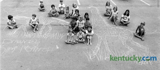 Neighborhood kids sit around a chalk drawing 13-year-old Kim Northrop made on the parking lot of the Cloister Apartemtns on Pimlioc Parkway in Lexington July 29, 1976. The kids blocked off traffic to the parking lot so a photographer could get a picture of the zebra and giraffe. Photo by Ron Garrison | staff