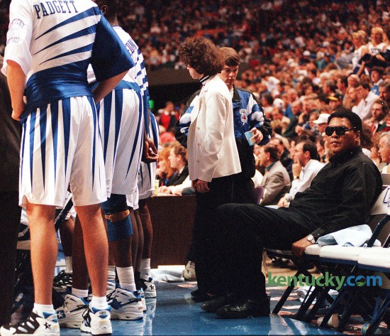 Three-time heavyweight boxing champion Muhammad Ali sat on the Kentucky bench during the Cats' game against Florida, Feb. 18, 1995 at Rupp Arena. Ali attended the game as part of a one-day promotional visit to Lexington for a play, Ali, which ran later that month at the Opera House. A playful Ali met the UK players in the locker room before the game. "He said I'll take you all on," Jeff Sheppard said. Ali also threw some punches. "I jabbed at Anthony Epps," Rodrick Rhodes said. "He told Epps he reminded him of Joe Frazier." UK coach Rick Pitino noted that the UK players were too young to remember Ali in his fighting prime. "For me, personally, it was a thrill of a lifetime," the UK coach said of Ali's presence on the bench. Ali and Sheppard shared a laugh while the game neared its dramatic finish. With 1:23 left and the Cats ahead 77-75, Sheppard was fouled but had to leave the game because of blood on his nose. Chris Harrison entered the game and made both free throws. As Harrison shot and team physician Dr. David Caborn worked on a cut on Sheppard's nose, Sheppard turned to Ali and said something. Ali and Sheppard then smiled. "I told him I got punched in the nose," Sheppard said. Photo by Mark Cornelison | staff
