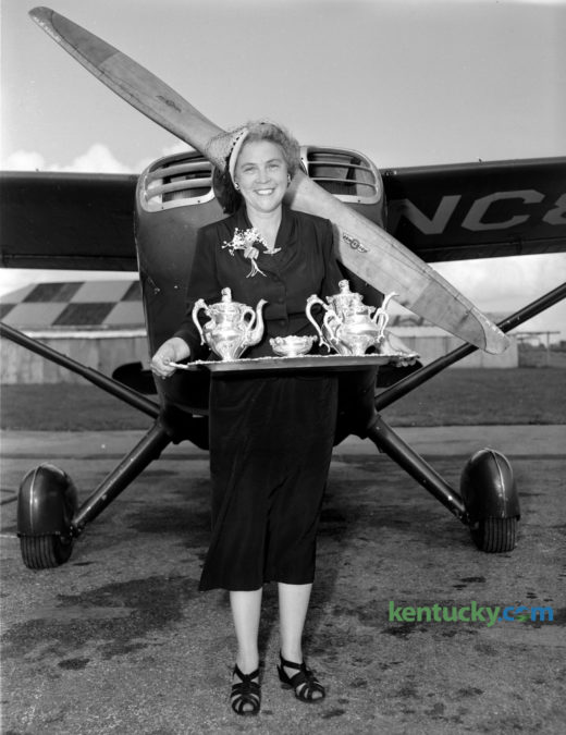 Portrait of Mrs. Greenwood Cocanougher standing in front of a small airplane, holding a silver tea set; August 1950.  She was awarded the tea set after winning the Jane Lausche Air Safety Trophy in the Powder Puff and Beau Derby, an efficiency race for women from Columbus, Ohio to Boston. Published in the Lexington Herald August 29, 1950. Herald-Leader Archive Photo