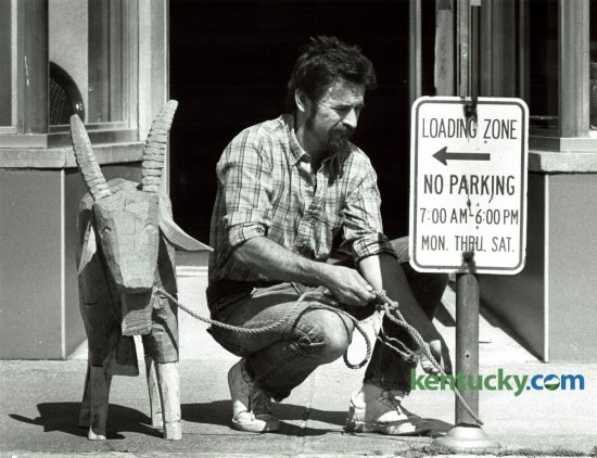 Adrian Swain tied a hand carved wooden goat to a no parking sign in front of his crafts shop in Morehead May 9, 1985. The goat, carved by Tom Sternal of Morehead, stood outside the shop to attract attention. Swain tied it up to discourage people from taking it. Photo by Ron Garrison | Staff