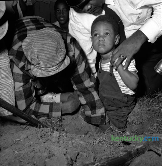 Three-year-old Calvin Doty Jr. waited to be freed after catching his foot in a post hole on October 16, 1951. Doty, son of Mr. and Mrs. Calvin Doty, Jr., 712D Charlotte Court was uninjured and excavated from the hole with the assistance of Aleza Jackson, left, and Patrolman Prather Walker.  Published in the Lexington Herald October 17, 1951. Herald-Leader Archive Photo