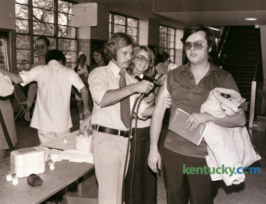 Donald Gross, right, a visiting assistant professor of political science at the University of Kentucky, stared straight ahead as he got his swine-flu shot October 28, 1976 at Memorial Coliseum from Paul Merkel, a state health department worker. Volunteer Judy Irvin, center, kept his sleeve up. This was the first of five local clinics for swine-flu shots for the general public. An estimated 5,000 people came to coliseum the first night and the health department expected to inoculate about 125,000 people before the program ended. Photo by David Perry | Staff