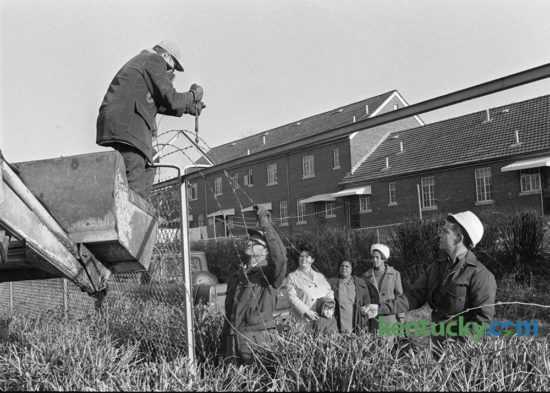 An eight-foot fence that separated blacks and whites since 1939 in the Blue Grass-Aspendale Housing Project comes down January 30, 1974. Taking down the barbed wire are, left to right, Jay Martin, Warren Gerton and Earl Osten, supervisor. Looking on are, left to right, residents, Mrs. Ruby Anderson and her son Steve; Mrs. Edith Hines, president of the Residents Council and Mrs. Lola Jones, also a council member. Photo by John C. Wyatt | Staff